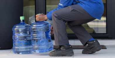 Person in a blue jacket carrying large water jug in right hand